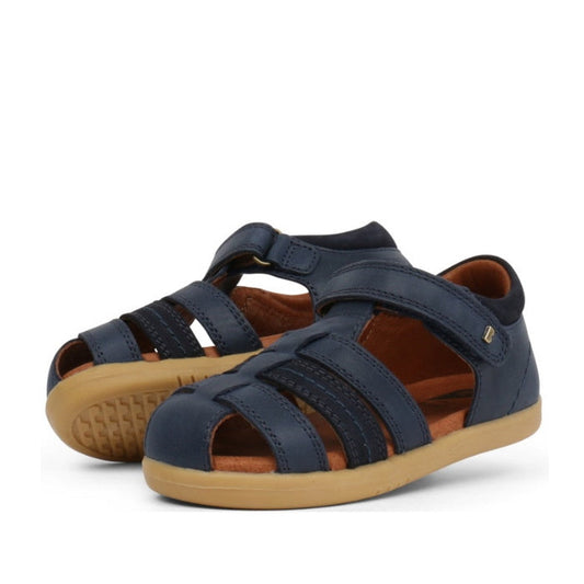 A picture of a pair of Bobux Roam sandals in the Iwalk range for toddlers aged 2 to 4 years. Closed toes in Navy with openings to allpw air flow. Heels supported wiyj a firm back to stop movement oin the heel.
