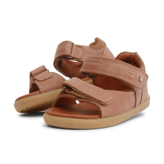 A pair of Bobux IWalk Driftwood Sandal Caramel Open Toe 633606A for kids with adjustable hook-and-loop straps and light brown rubber soles, displayed on a white background.