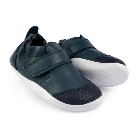The Bobux Explorer Go First Walking Trainer Navy 501012B are dark blue toddler leather shoes with white rubber soles and Velcro straps, ideal as first walking shoes, pictured on a white background.