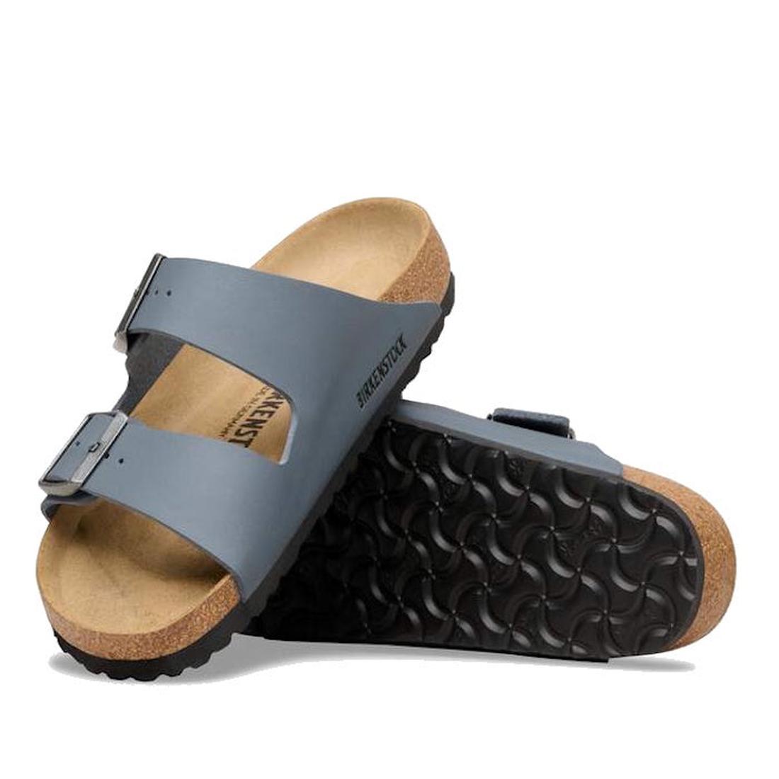 A pair of BIRKENSTOCK Arizona Birko Flor Balsat Grey Regular Width 2 Strap Sandals with cork-latex footbeds and black textured soles—one upright, the other leaning to showcase the sole’s distinctive pattern.