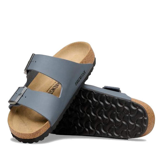A pair of BIRKENSTOCK Arizona Birko Flor Balsat Grey Regular Width 2 Strap Sandals with cork-latex footbeds and black textured soles—one upright, the other leaning to showcase the sole’s distinctive pattern.