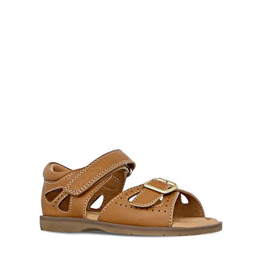 The Clarks Carrie Tan Leather Girls Sandal features a single tan design with buckle and hook-and-loop strap, decorative cutouts, stitching details, flat sole, and open toe, displayed against a white background.