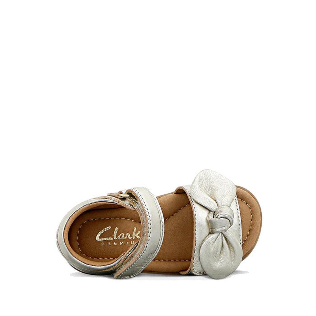 The Clarks Samara Toddlers Gold Leather Sandal (D Narrow Width) features a metallic gold leather upper, knotted bow on the front strap, Velcro ankle strap, branded “Clarks Premium” insole, and tan sole. Displayed on a white background., 40541, 93360782351
