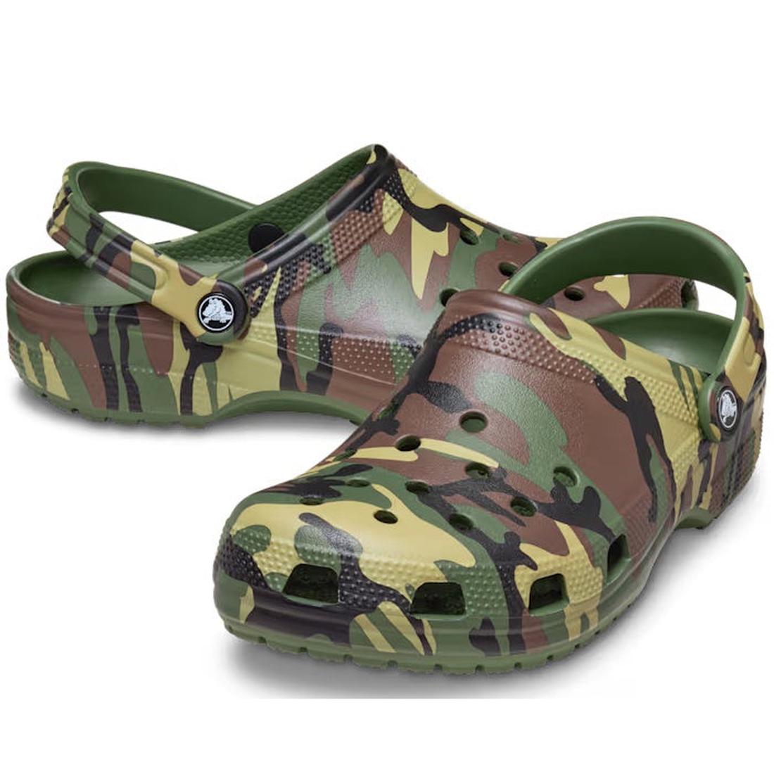 The Crocs Classic Clog Camouflage Adults Unisex features a green, brown, and tan camo print, adjustable heel straps, and can be customized with Jibbitz charms. Shown on a white background.