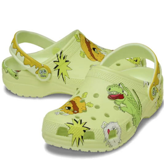The Crocs Kids - Classic Clog Glow Silly Slime Green (Junior Youths Sizes) features a pale yellow upper decorated with green monster and food-themed cartoon charms, such as alligators and burgers, plus playful slime accents and yellow comic-style bursts o