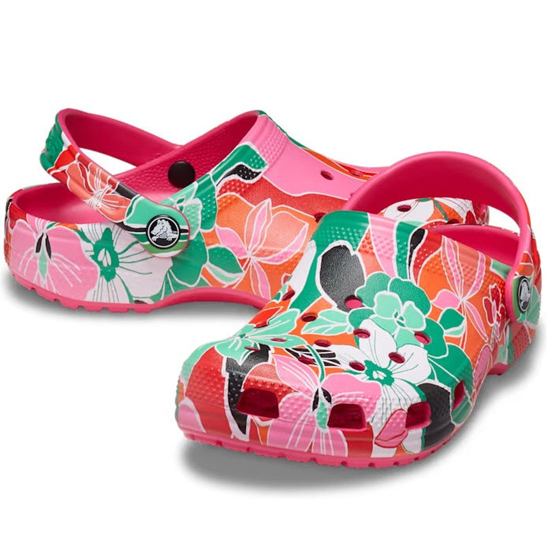 The Crocs Kids Youths Classic Clog K Woodcut Floral Print features a vibrant pink, red, green, and white floral pattern, adjustable heel strap, toe ventilation holes, Crocs Comfort, and can be customized with Jibbitz charms.