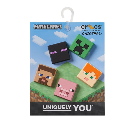 The Crocs Jibbitz 5 Pack - Minecraft features pixelated charms of Creeper, Enderman, Steve, Alex, and a pig to decorate your Crocs. Shown against a blue sky and grass block background.