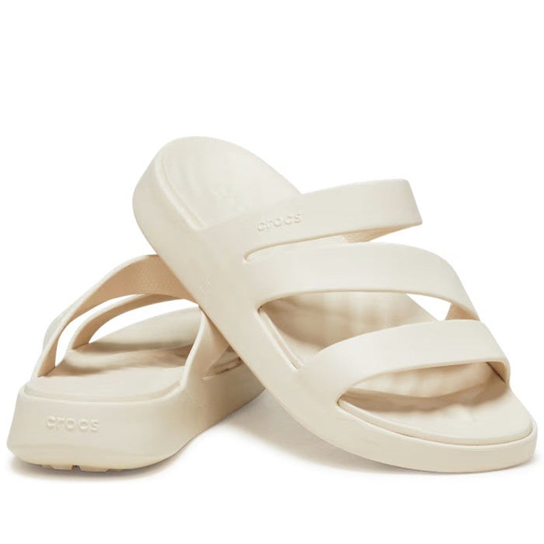 A pair of Crocs - Womens Getaway Strappy Slide Sandals in Stucco Bone, featuring two thick straps and a slightly raised sole with Free Feel Technology, are positioned with one sandal leaning on the other.