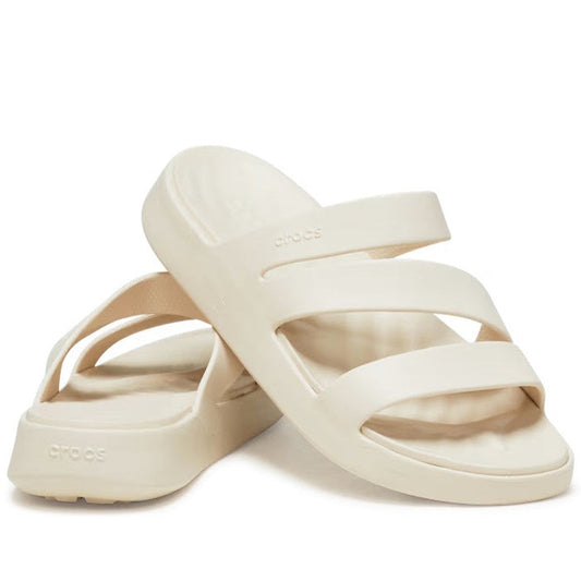 A pair of Crocs - Womens Getaway Strappy Slide Sandals in Stucco Bone, featuring two thick straps and a slightly raised sole with Free Feel Technology, are positioned with one sandal leaning on the other.