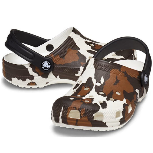 The Crocs Kids - Youths Classic Clog K Cow Print White Sandals feature a black and white cow print, black heel straps, and ventilation holes; perfect for young fans of Western-style footwear.