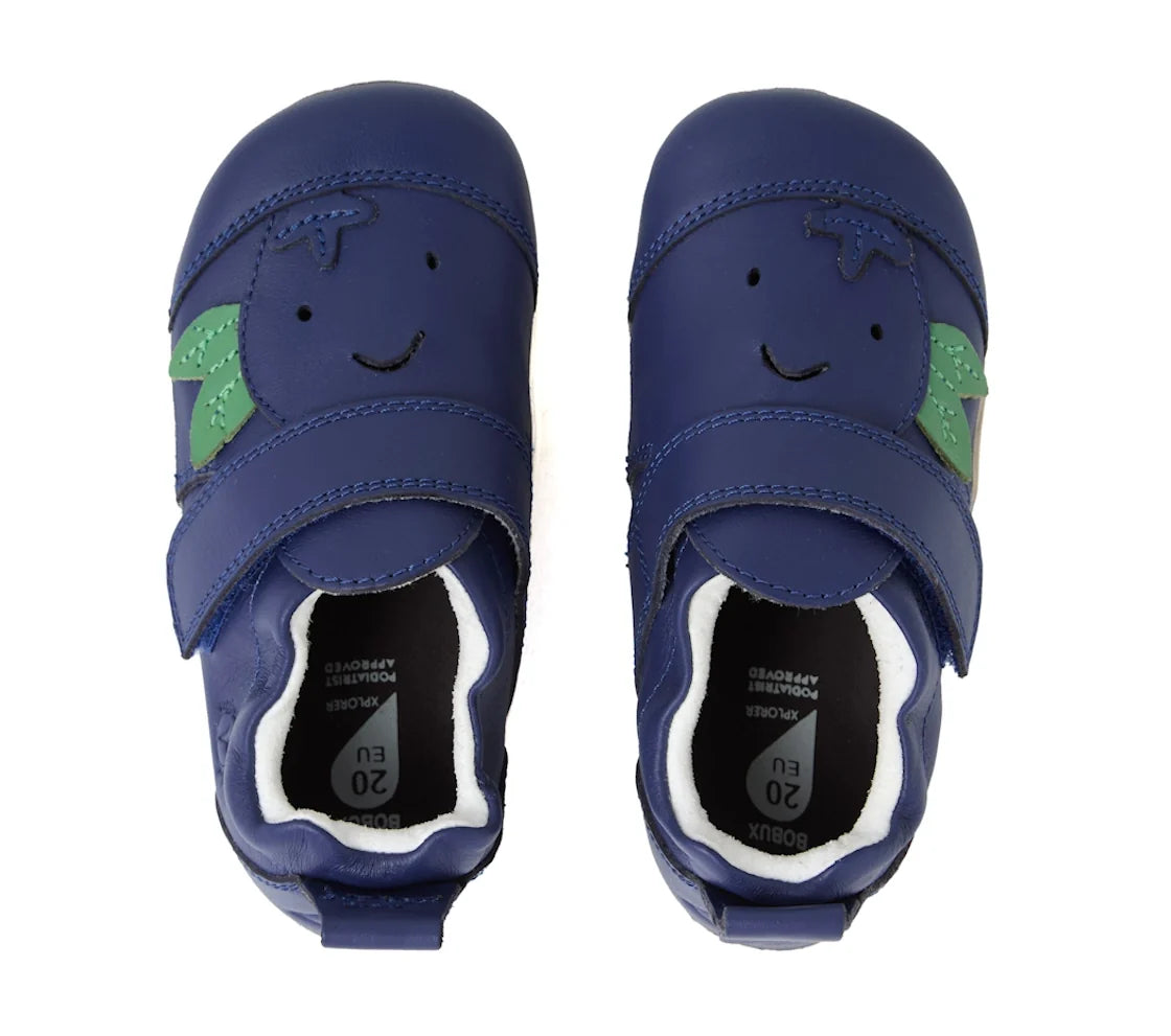 A pair of Bobux XP Explorer Little Sprouts Blueberry Dash First Walker Blue toddler shoes, featuring smiling faces and green leaf designs, viewed from above. These blue leather baby shoes have hook-and-loop straps, flexible soles for comfortable movement,