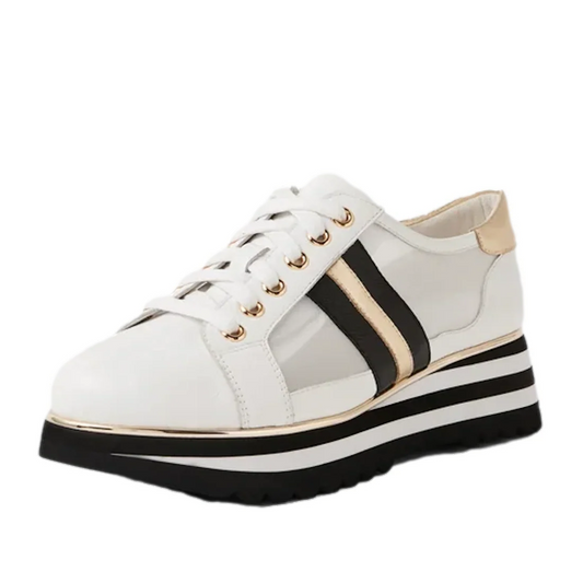 The Django & Juliette Eminta Platform Shoe is a white women’s lace-up sneaker featuring gold eyelets, black and gold side stripes, sheer leather side panels, and a bold black-and-white striped platform sole.