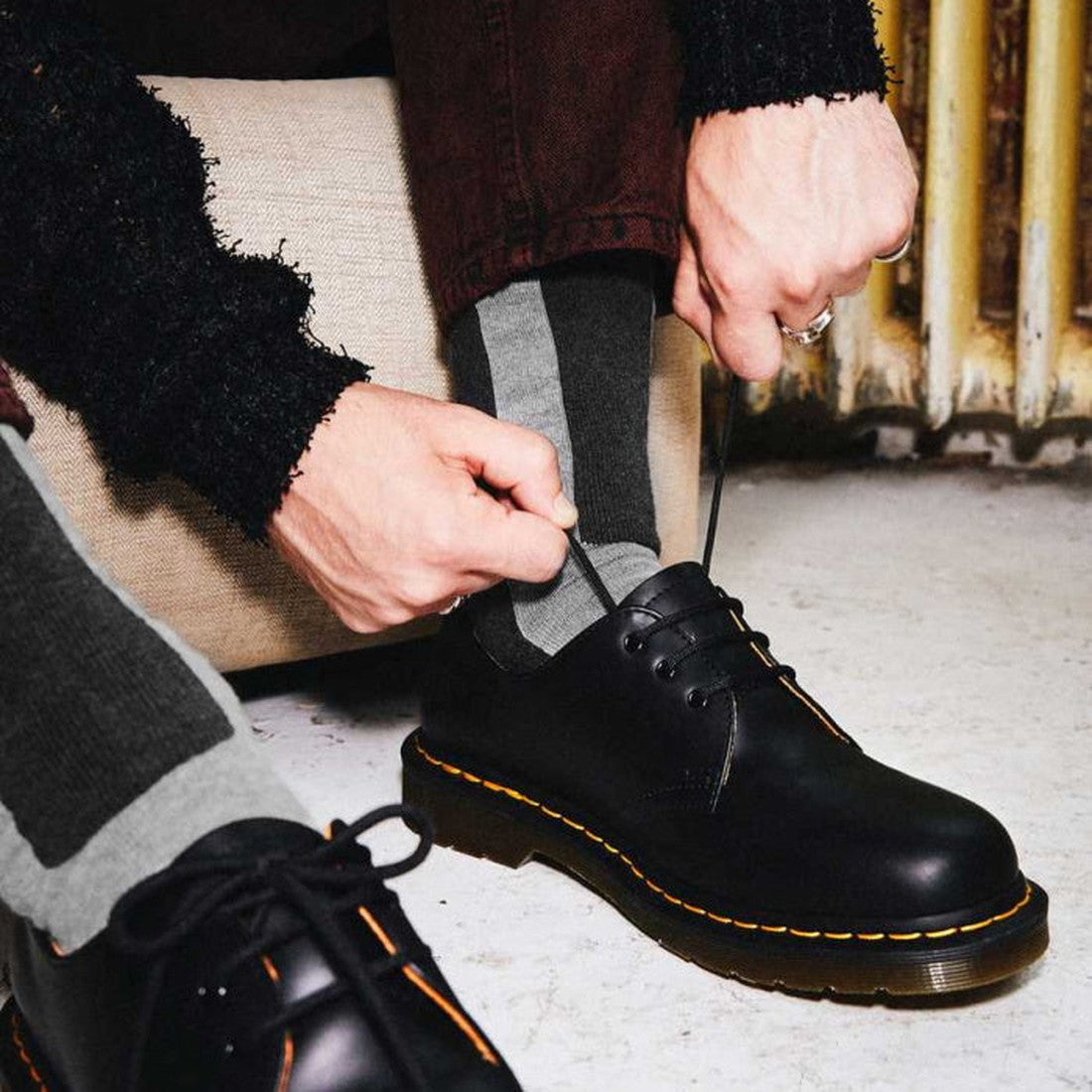 A family member ties sturdy laces on the Dr Martens Double Doc Sock Unisex Charcoal boot, featuring a black leather finish, bright yellow stitching, and a durable sole.  ksnz, 190665440324, 190665440317