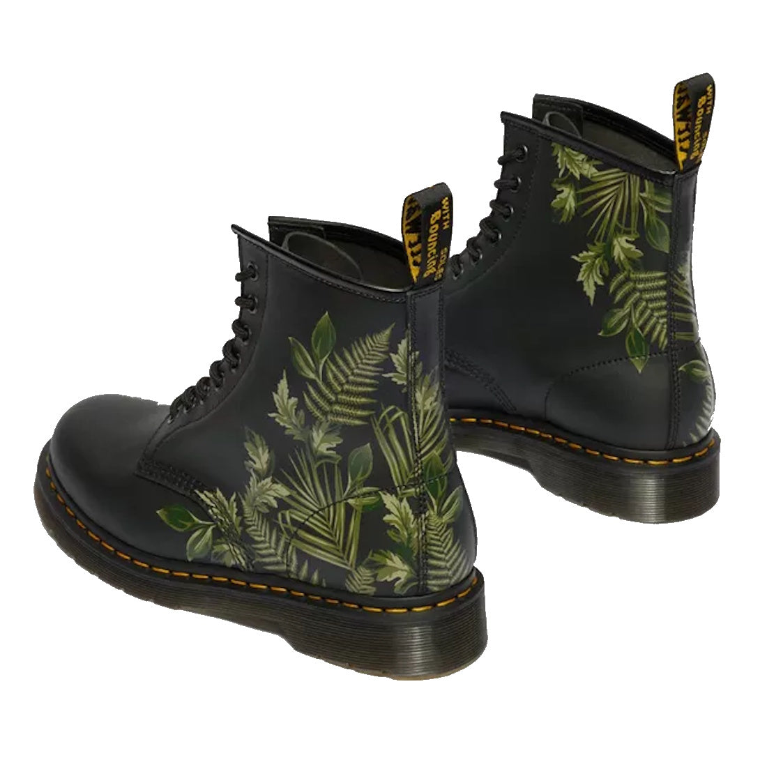 The 1460 Dr Martens Smooth EverGreen Leather 8 Up Boot features green fern and leaf designs on a black background, classic yellow stitching, black soles, lace-up front, and branded yellow pull tabs.