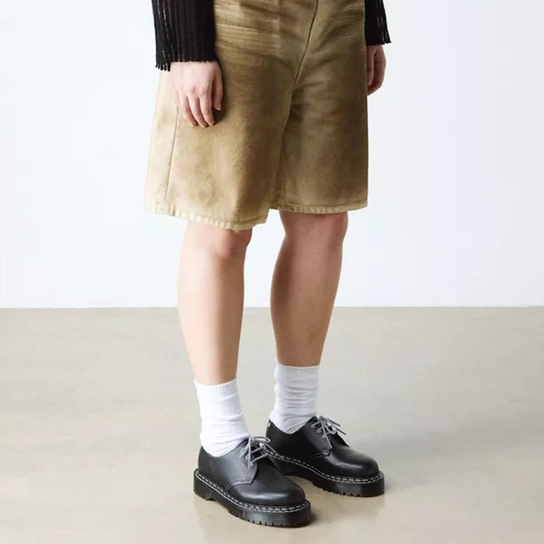 Person wearing tan corduroy shorts, a black long-sleeve top, white socks, and Dr Martens 1461 Bex WDS White Stitching Black Sendal Oxford Shoes, standing on a light-colored floor against a plain background., 50357, 190665781496, 190665781502, 190665781526