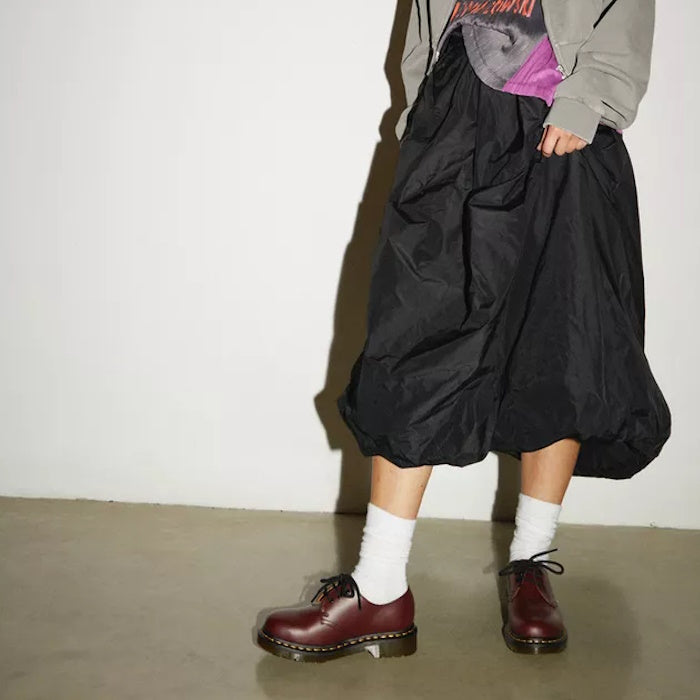 A child wears comfy clothes and Dr Martens 1461 Cherry Red Oxford Shoes with sturdy soles and classic lace-up, standing by a white wall.  ksnz, 800090826524, 800090798456, 800090798470, 800090798487, 800090798494, 800090798517, 800090798524