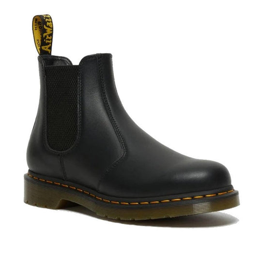 The right foot of a Dr Martens black leather 2976 Chelsea boot with elastic side panels and a pull tab featuring yellow branding. In Nappa a sfter and not too shiny leather. The boot has a sturdy sole with yellow stitching along the edge, giving it a sign