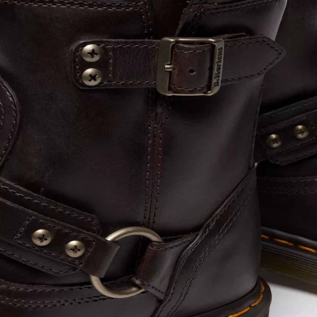 Close-up of Dr Martens Anistone Harness Bex Crazy Dark Brown Horse Biker Boots with a slightly glossy, textured leather, metal buckles, rivets, circular ring detail, and orange stitching accenting the sole., 49399, 190665745689, 190665745696, 190665745719