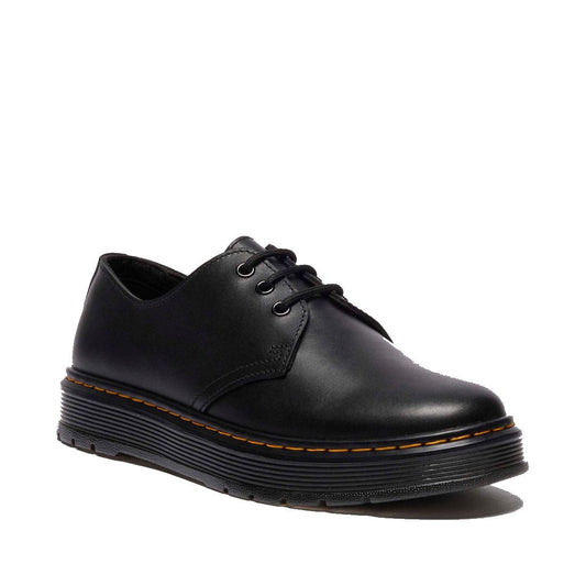 The Dr. Martens Brookline Dark Black Lusso Leather Shoe is a lace-up oxford featuring lightweight leather, a thick ridged sole, and signature yellow stitching along the edge.