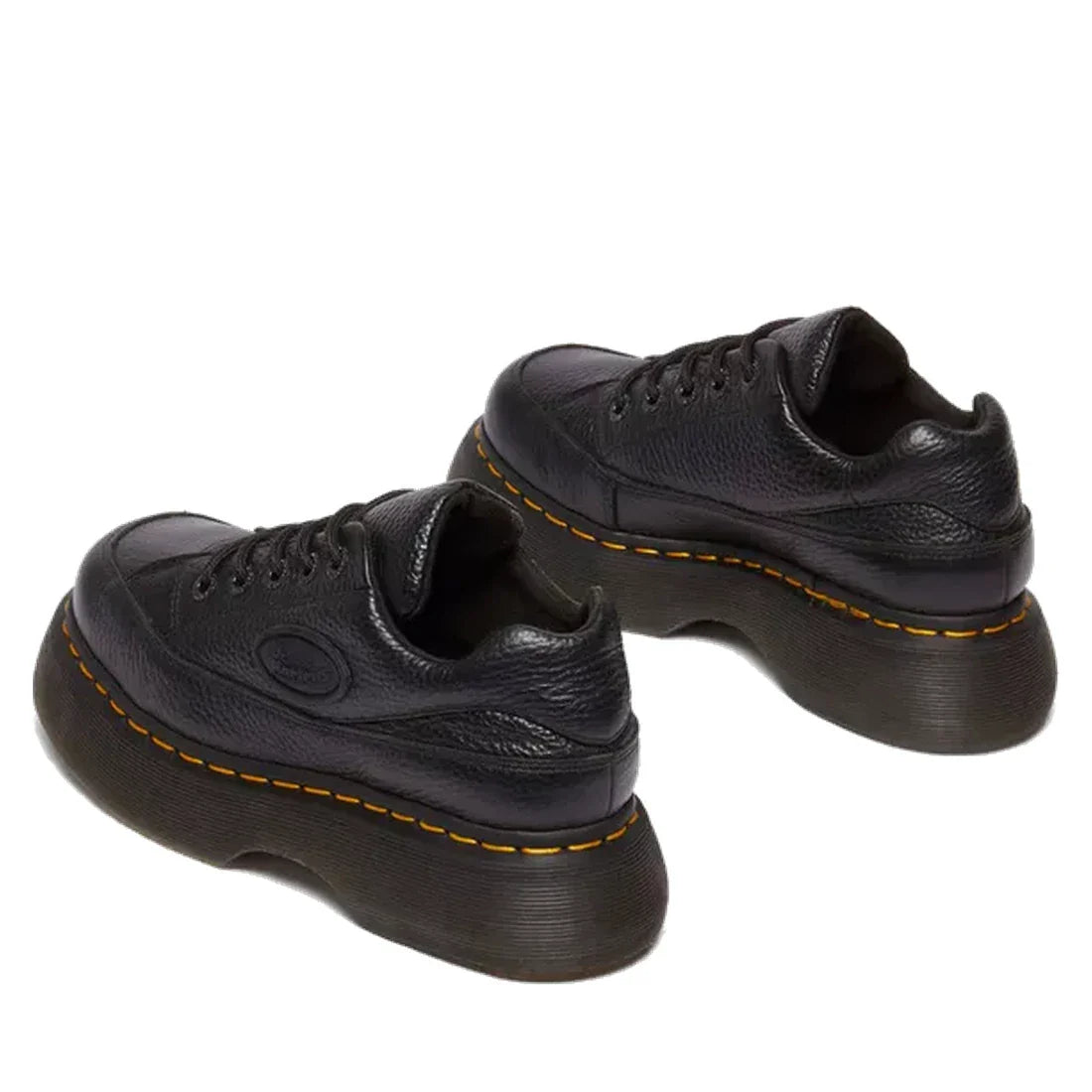 The Dr Martens Buzz 5i Milled Nappa Black Leather 5 Eye Shoe features black milled Nappa leather, thick textured platform soles, signature yellow stitching, and Goodyear-welted construction, shown from a rear side angle., 51613, 190665702798, 190665702804
