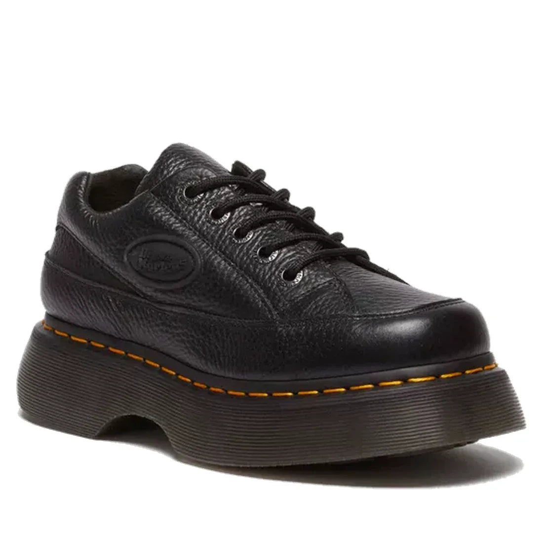 The Dr Martens Buzz 5i Milled Nappa Black Leather 5 Eye Shoe features textured black leather, black laces, a thick grooved sole, and signature yellow stitching around the Goodyear-welted sole.