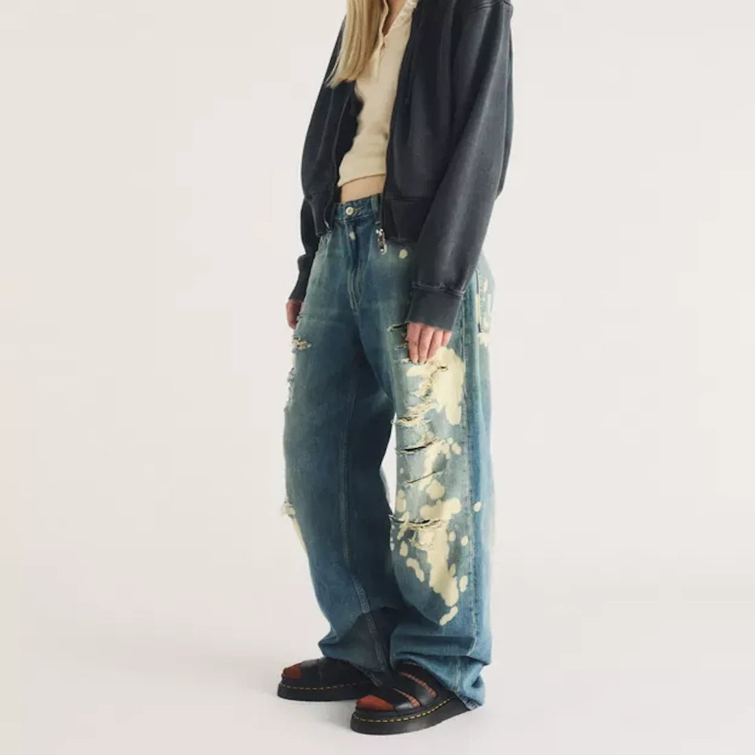 A person wearing wide-leg distressed jeans with bleach spots and black Dr Martens Clarissa II Quad Platform Sandal sandals.