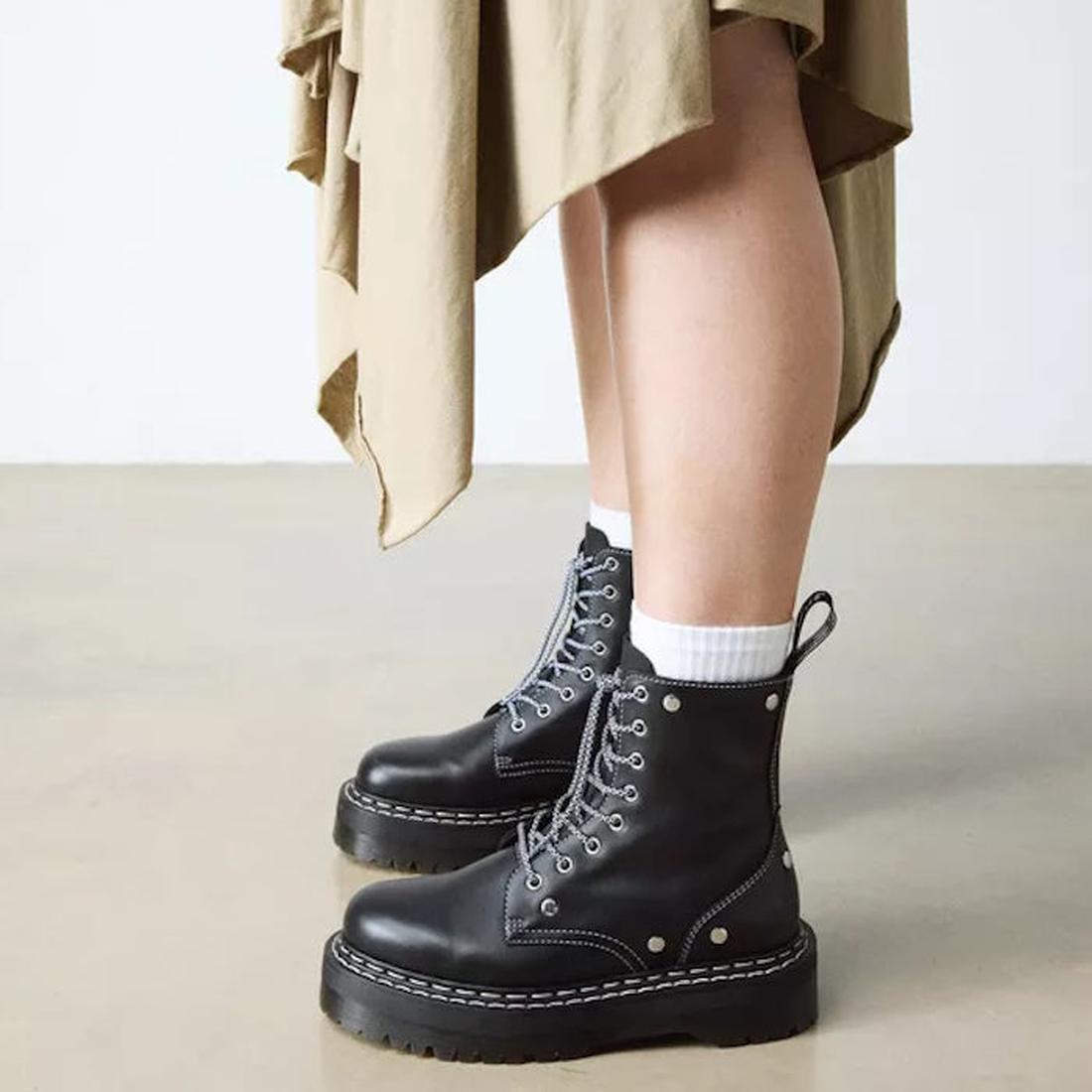 A person wearing Dr Martens Jadon WDS White Stitching Hardware 8 Eye Boot Black with thick soles, white socks, and a beige asymmetrical skirt stands on a light floor, highlighting the platform silhouette., 50347, 50348, 190665775471, 190665775488, 1906657