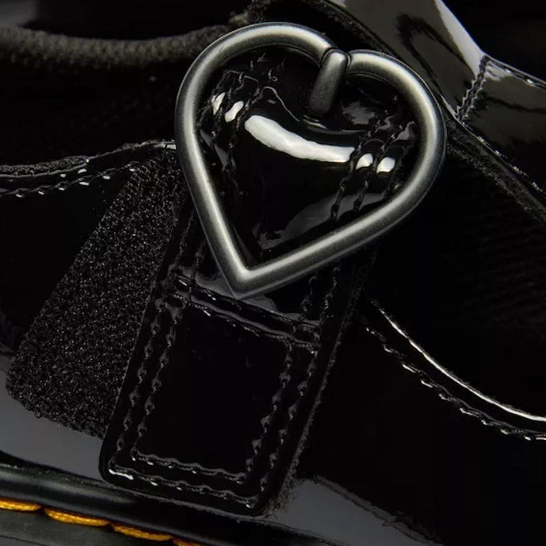 Close-up of the Dr Martens kids Polley II Heart T Bar Junior in black patent, showing a shiny strap with a heart-shaped buckle, detailed stitching, and glossy finish—perfect classic-inspired school shoes., 50432, 50433, 190665786743, 190665786750, 1906657