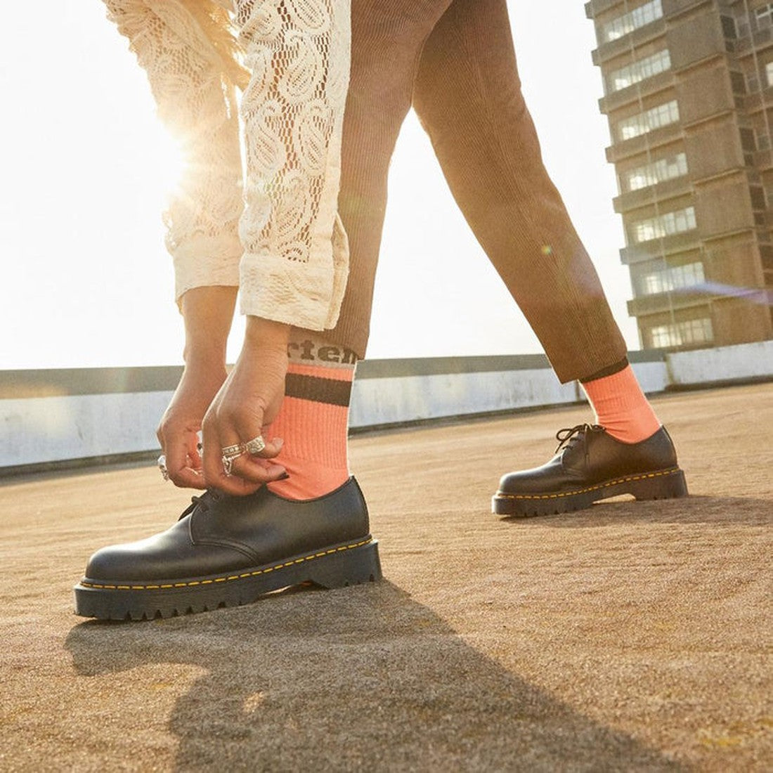 A parent ties the laces of classic black leather shoes with sturdy soles, paired with cozy beige Dr Martens Organic Socks Athletic Logo.  ksnz, 190665558487, 190665558470