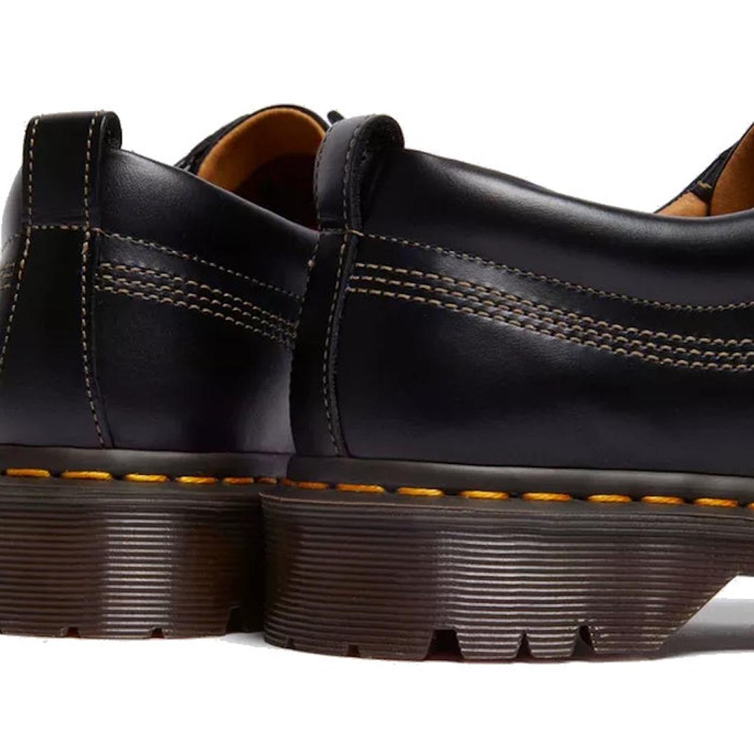 Close-up of the back and side of two Dr Martens Lowell Moc Toe Black Leather Shoes in aniline leather, featuring thick brown ridged soles and signature yellow stitching., 50395, 50396, 50397, 50398, 50399, 190665668940, 190665668957, 190665668971, 1906656