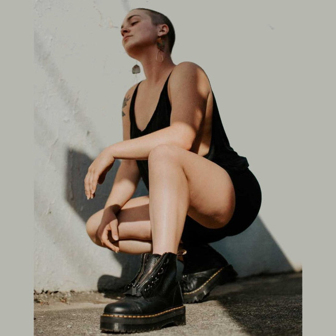 A cheerful adult relaxes by a bright wall, wearing Dr Martens Sinclair Boot in black leather with zippers, thick sole, and laces.  ksnz, 190665055955, 190665055962, 190665055979, 190665055986, 190665055993, 190665056006, 190665056013