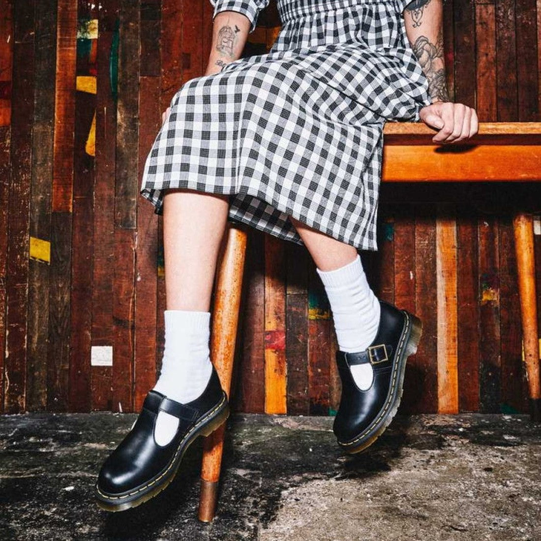 A womens in a black white ginham dress sitting on a chair and swinging her legs wearing Dr Martens Polley Mary Jane T-Bar shoes in black smooth leather. Also styling with white ankle socks.
883985498242,
883985498259,
883985498266,
883985498273,
883985498