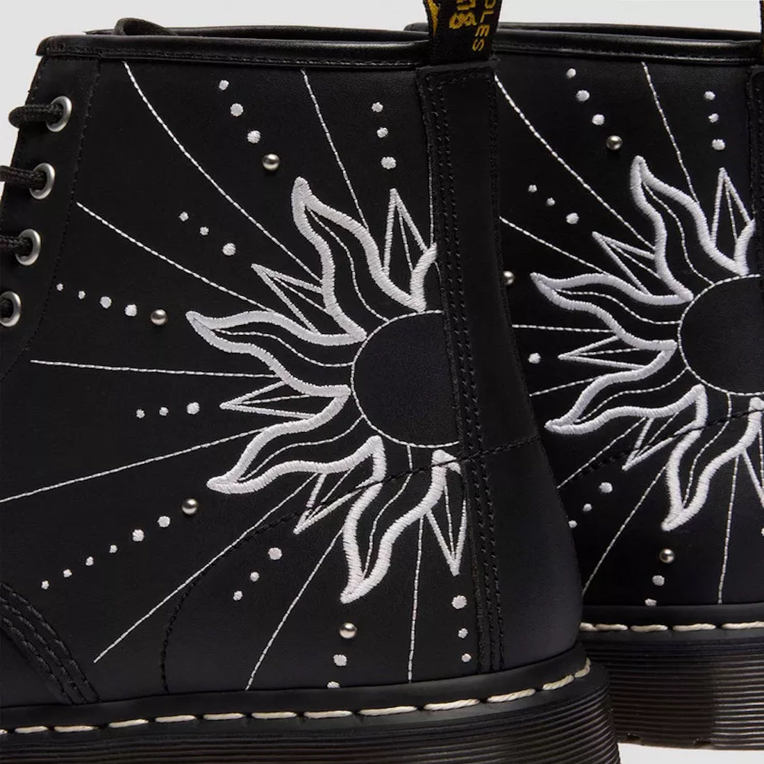 Close-up of the Dr Martens 1460 Genix Solar Flare Black 8 Up Eye Boot, made in Genix Nappa leather with black uppers, white embroidered sun and ray details, silver studs, and classic stitching for a bold artistic look., 190665742824, 190665742831, 1906657