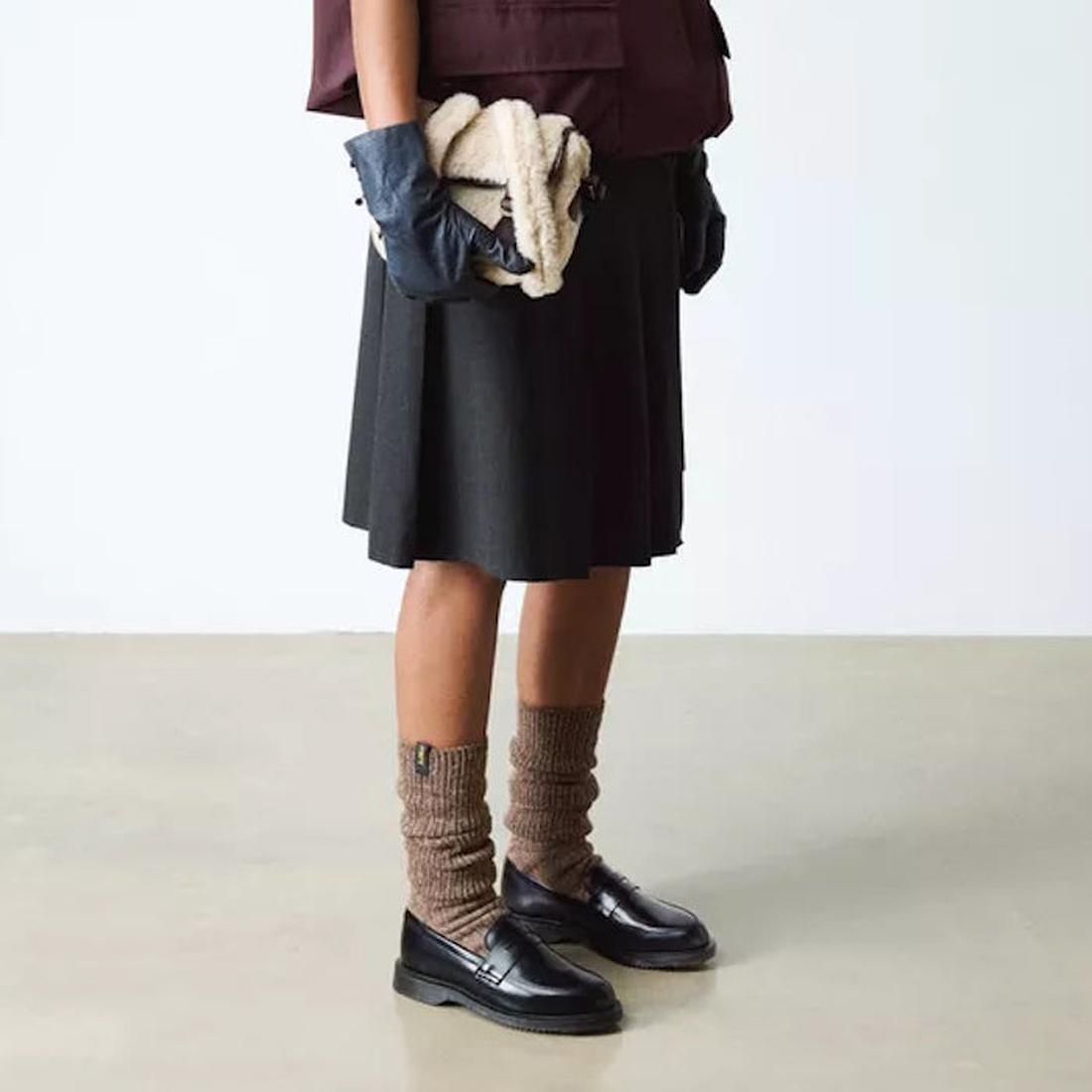 Standing on a light floor, this person wears a dark pleated skirt and brown leg warmers with comfy Dr Martens Temara Black Leather Loafers, featuring a sturdy sole and easy slip-on design—perfect for stylish families. Upper body not visible.  ksnz, 190665747485, 190665747492, 190665747515, 50757, 50758