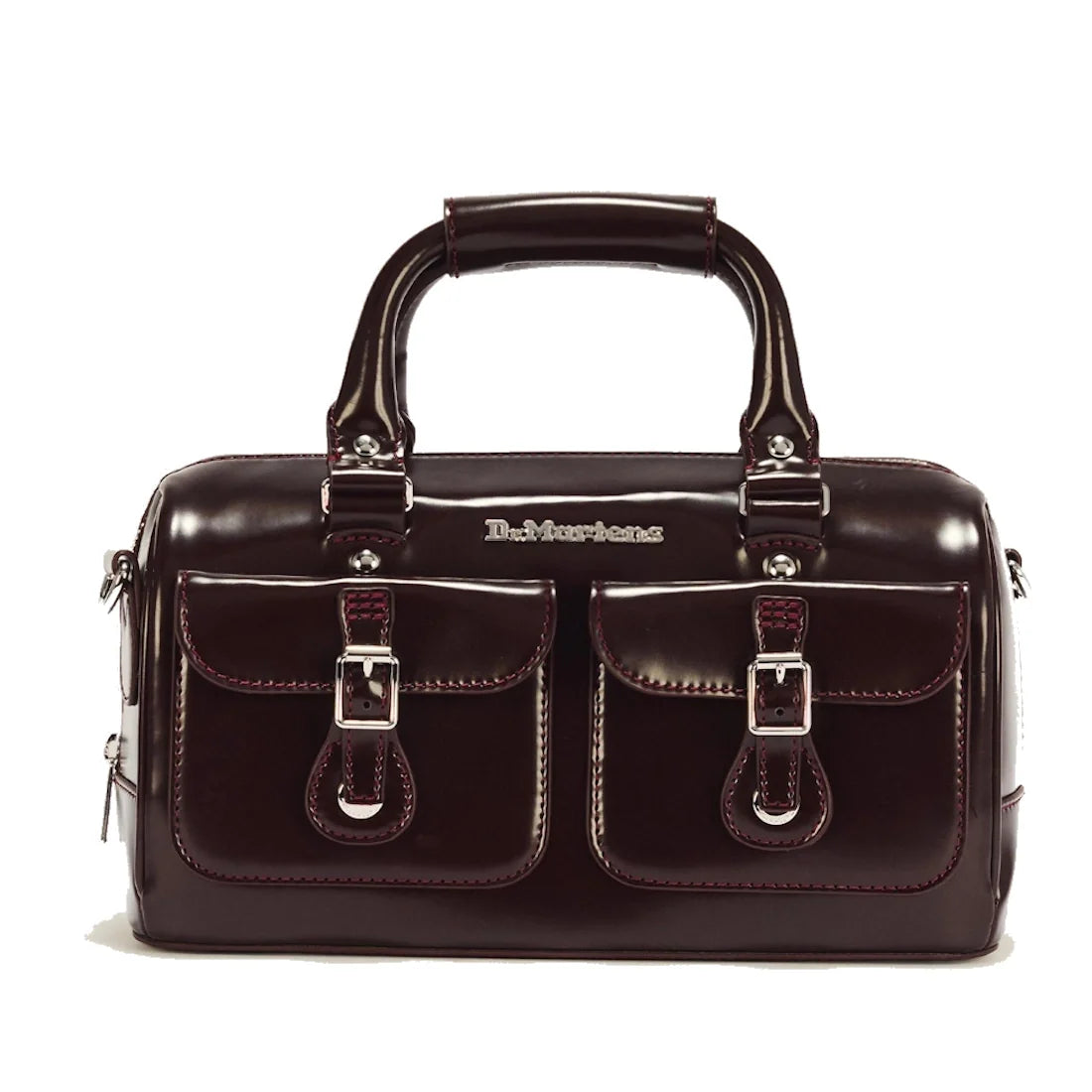 A glossy dark brown handbag inspired by the Dr Martens handle bag design, featuring two front pockets, buckle details, silver hardware, and a sturdy top handle. The brand name is visible above the pockets.