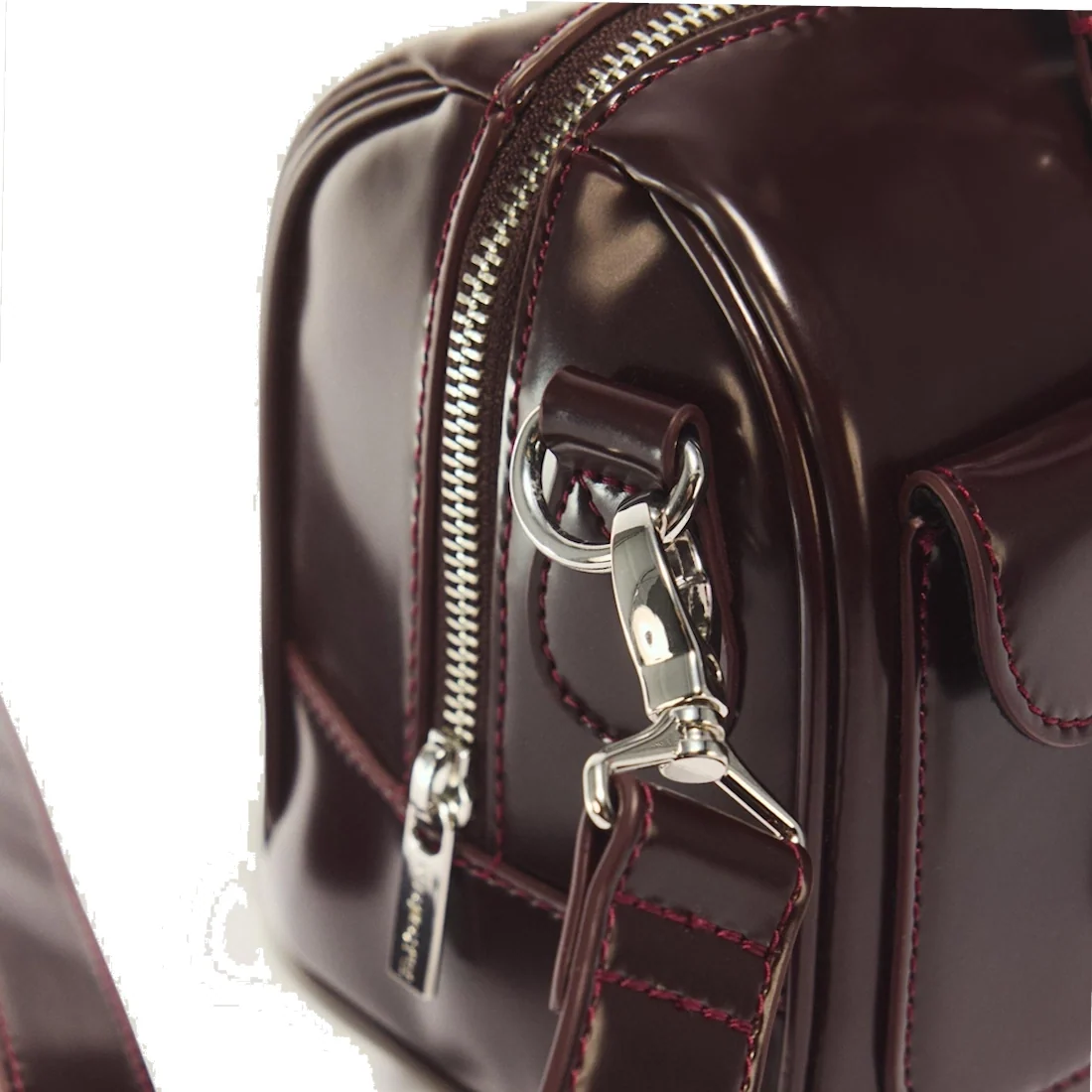Close-up of the Dr Martens Top Handle Bag in Cherry Red Oxford Rub Off, featuring glossy burgundy leather with silver hardware, including a zipper, detailed stitching, and a metal clasp on the strap—an elegant accessory showcasing the signature oxford rub