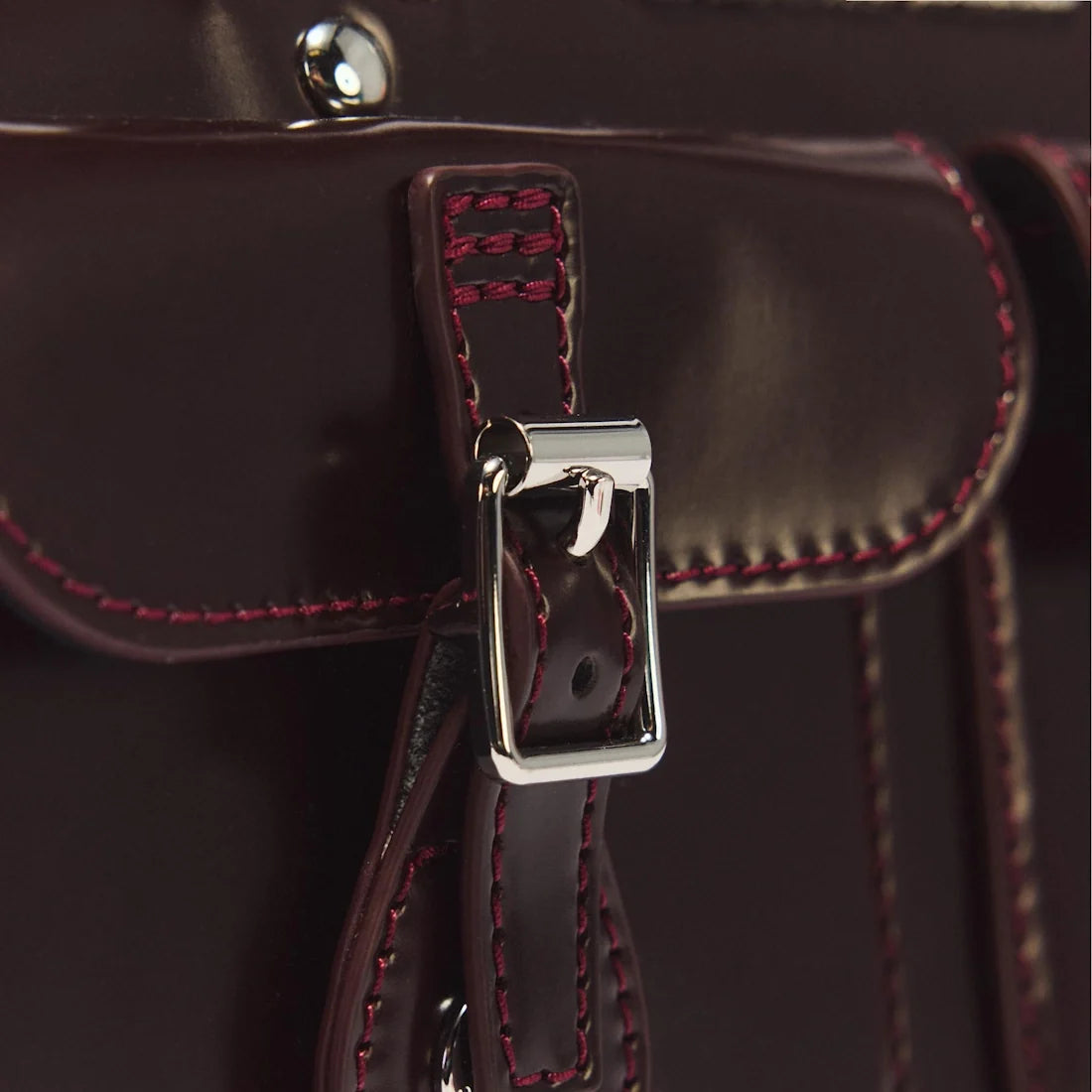 Close-up of the Dr Martens Top Handle Bag in Cherry Red Oxford Rub Off leather, featuring a shiny silver buckle and maroon stitching, showcasing detailed craftsmanship and the rich texture inspired by the classic oxford rub off finish.
