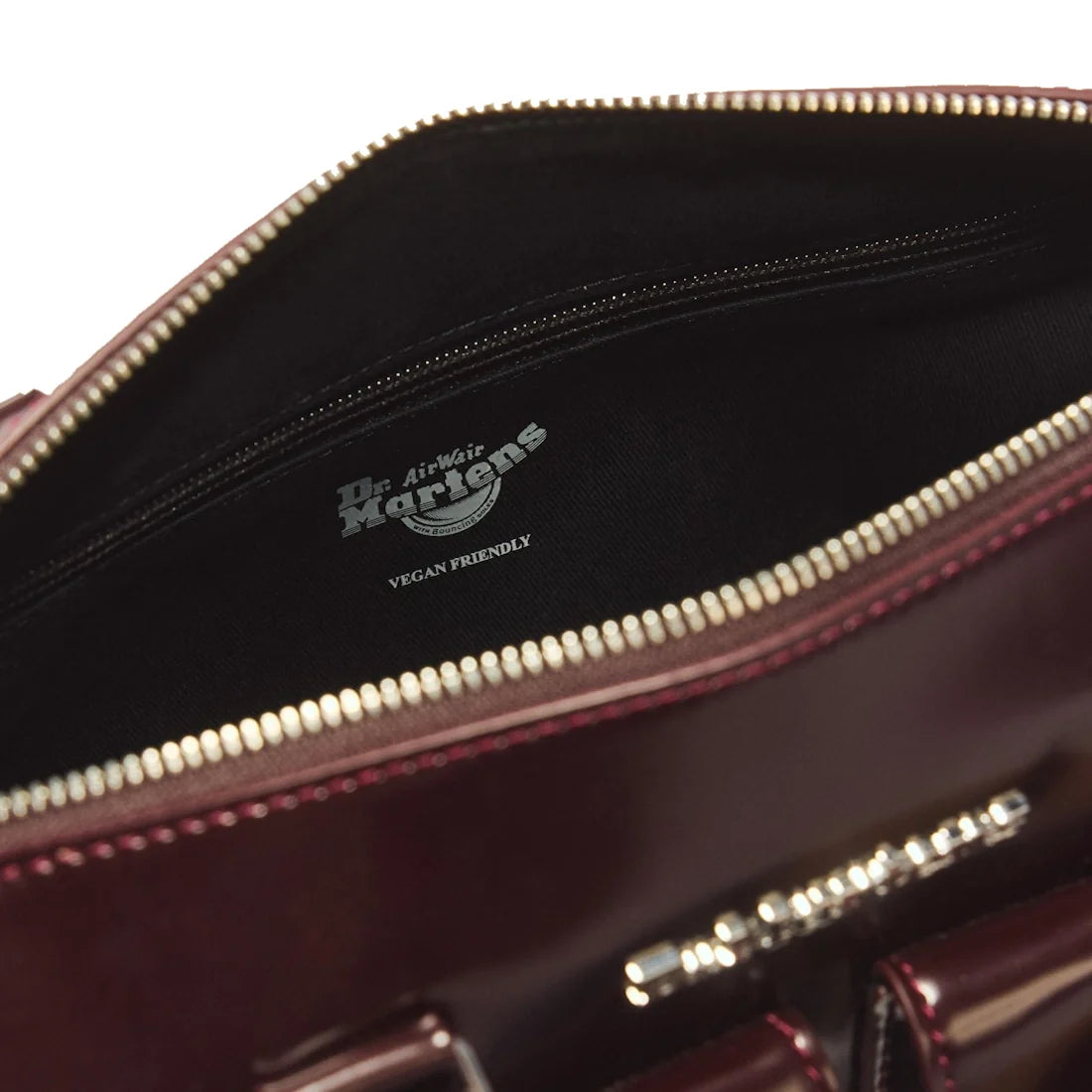 Close-up of an open Dr Martens Top Handle Bag Cherry Red Oxford Rub Off with a visible zipper, showing the inside label reading Dr. Martens AirWair VEGAN FRIENDLY on the black fabric lining.
