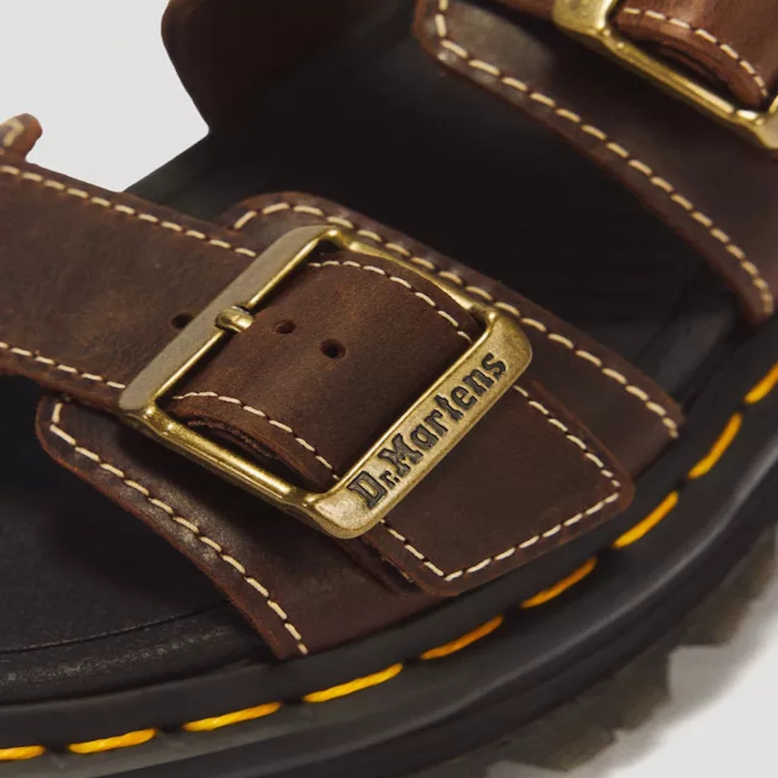 Close-up of the Dr Martens Zebzag Crazy Horse Brown 2 Strap Sandal featuring gold buckles—one engraved with Dr. Martens—and signature yellow stitching circling the thick black air-cushioned platform sole., 52549, 190665818604, 190665818611, 190665818635, 