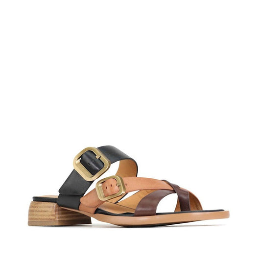The EOS Teia Black/Brandy/Coconut Low Heeled Sandal Slide features black, brown, and tan leather crisscross straps, two large gold buckles for adjustment, a stylish low stacked wooden block heel, and a sleek contemporary design.