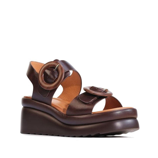 The EOS Menorcas Chestnut Brown Leather Wedge Sandal features thick straps, round buckle details, an open toe, chunky platform sole, visible stitching, a ridged outsole, and excellent arch support for lasting comfort.