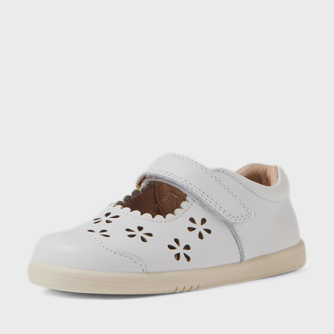 The Bobux IW Iwalk Toddlers Heather White Leather Mary Jane is a charming girls’ shoe featuring a hook-and-loop strap, scalloped edges, and delicate cut-out flower patterns on top. Crafted from smooth leather, it has a beige sole and a light brown inner l