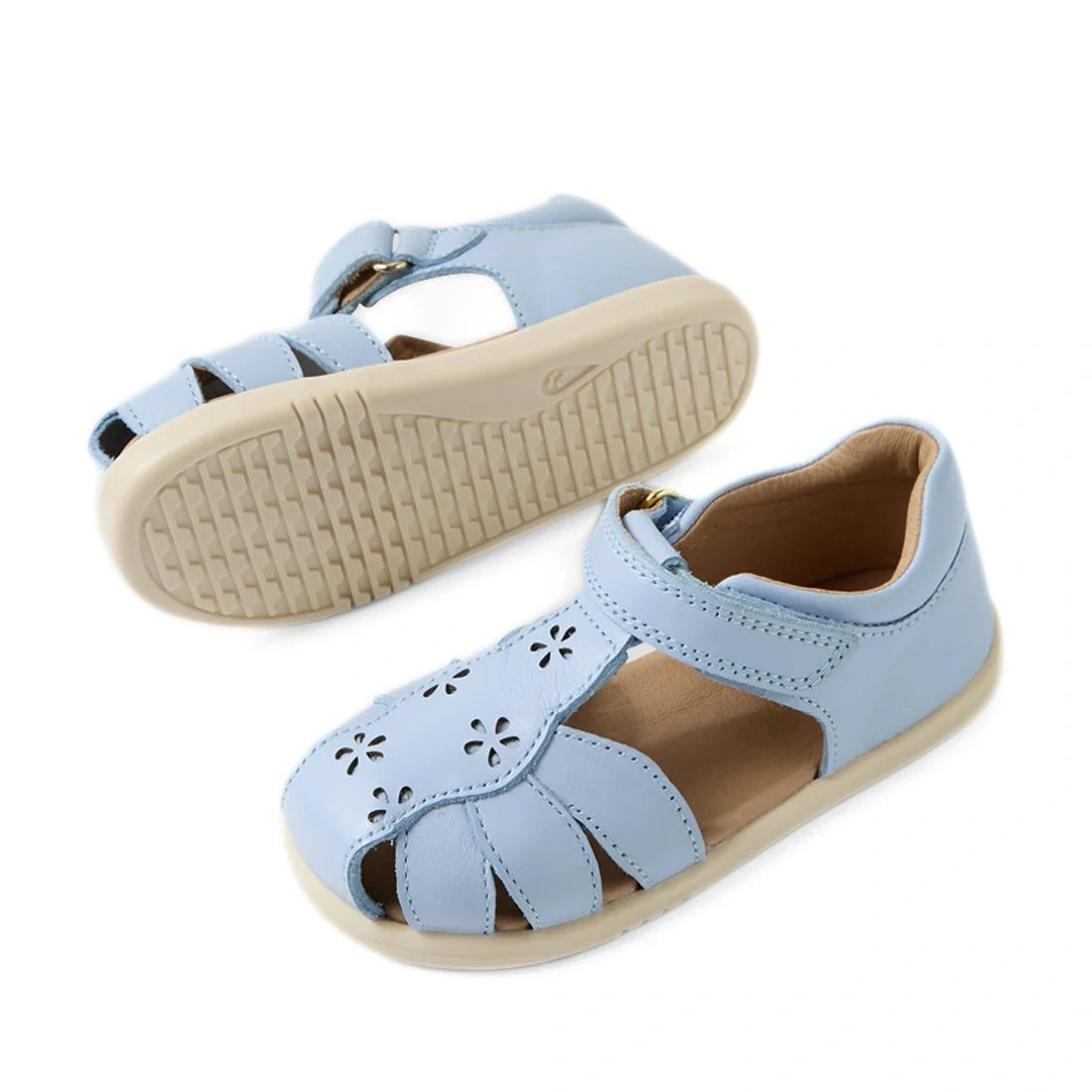 Introducing the Bobux IWalk Holly Toddlers Sandal in Skyway Blue: closed toe sandals for children with delightful cut-out flower motifs, a secure Velcro ankle strap, and beige rubber soles. Made from quick-drying leather, these sandals provide both comfor