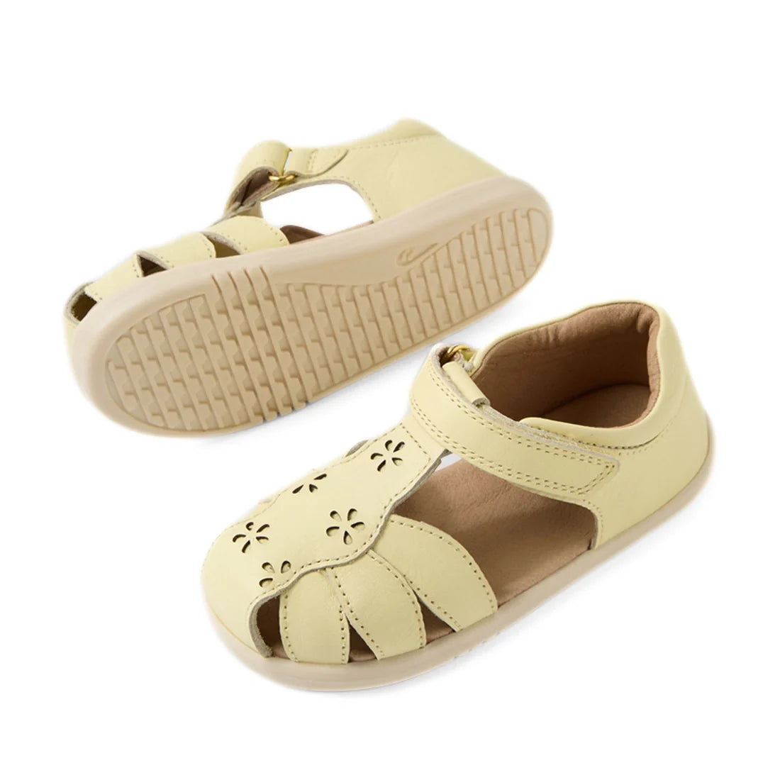 The Bobux IWalk Holly Toddlers Sandal in Wax Yellow features a light yellow closed-toe design for toddlers, crafted from quick-drying leather with delightful cut-out flower details. These sandals include a Velcro strap and flexible beige rubber soles. One