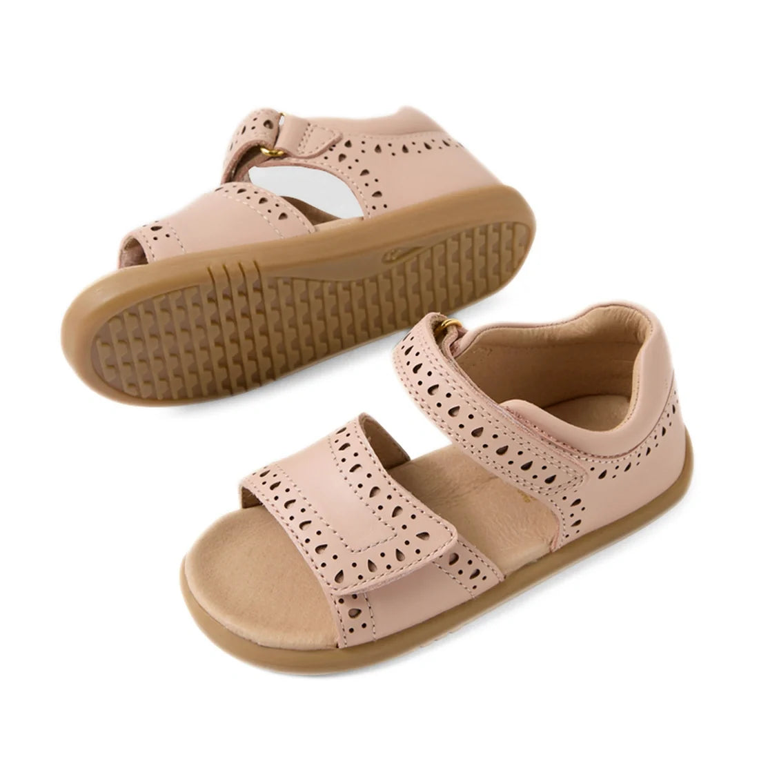 Two Bobux IWalk Logan Toddlers Sandals in Cameo Rose Pink, featuring an open toe, perforated decorative edges, tan soles, and hook-and-loop straps. One leather sandal is upright, while the other displays its textured sole., 9420074853172, 9420074853189, 9