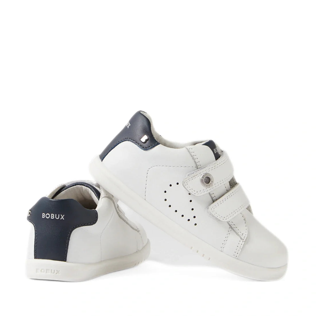 A pair of Bobux IW Iwalk Maverick Toddlers Leather Sneakers in white with navy blue heels and Bobux branding are displayed—one upright and one leaning to show both the side and back. These sporty children’s sneakers feature adjustable Velcro straps and a 