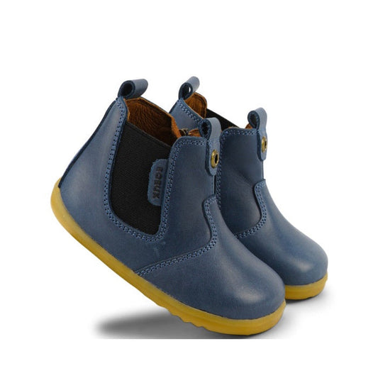 The Bobux Step Up Jodphur Boot Midnight Blue 721949A features blue leather, yellow soles, black elastic side panels, and front and back pull tabs—perfect unisex boots for first walkers.