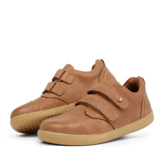 The Bobux Kid+ Port Shoe Caramel Tan 833002 features light brown leather, tan rubber soles, and two Velcro straps per shoe, shown against a white background.