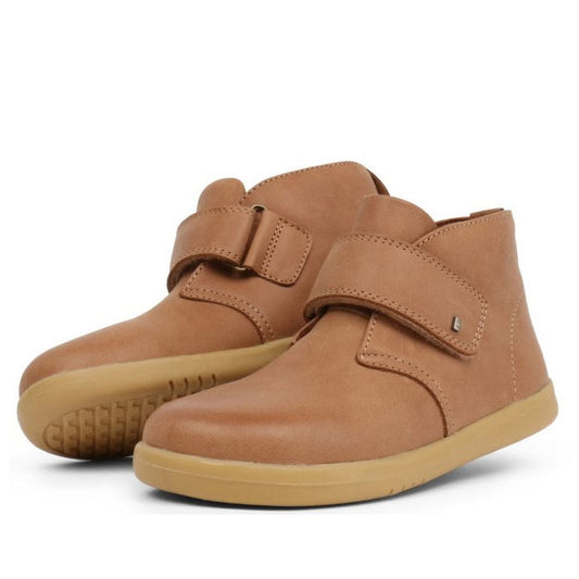 The Bobux Kid+ Desert Boot Caramel 830305Z features light brown leather high tops with beige rubber soles and a wide Velcro opening across the front, displayed against a white background.