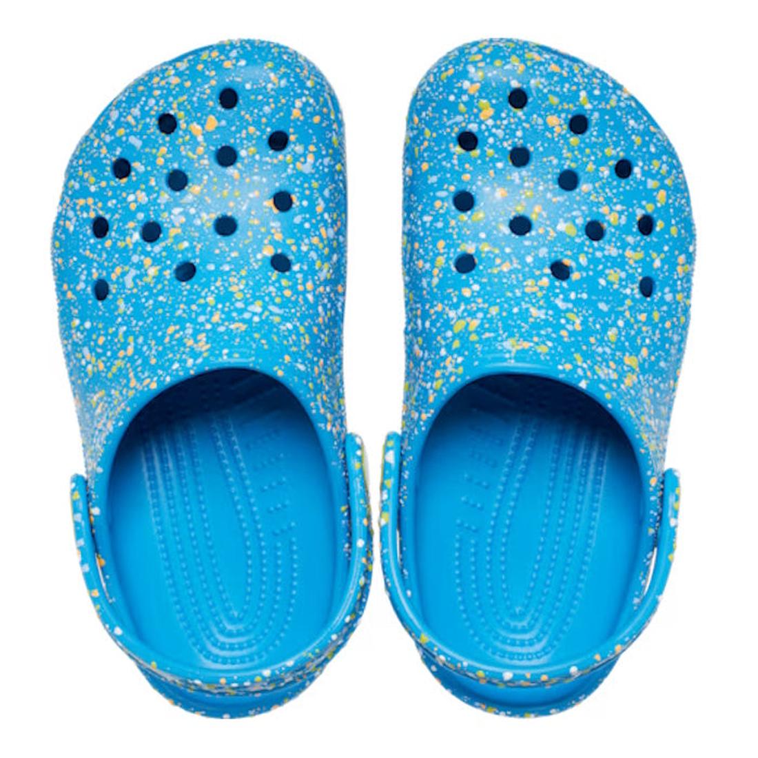 The Crocs Kids - Toddlers Classic Clog K Paint Splatter Print Blue Pink Multi features lightweight blue clogs for kids with colorful paint splatters, ventilation holes, and adjustable heel straps, shown from above on a white background., 47582, 1984452141